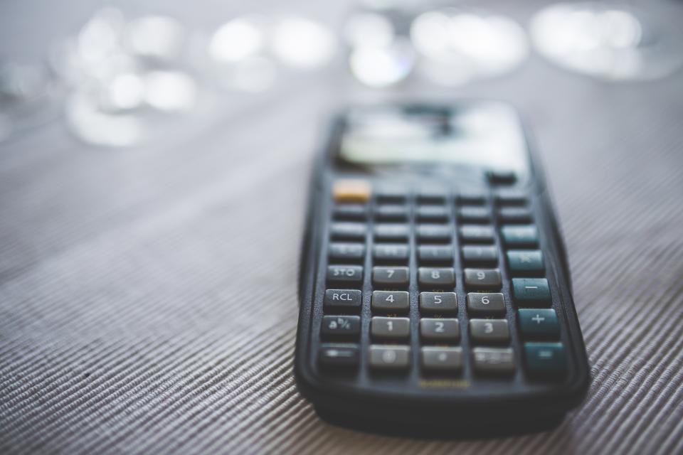 Close-up of a dark calculator on a gray textured table with soft blurred light behind it