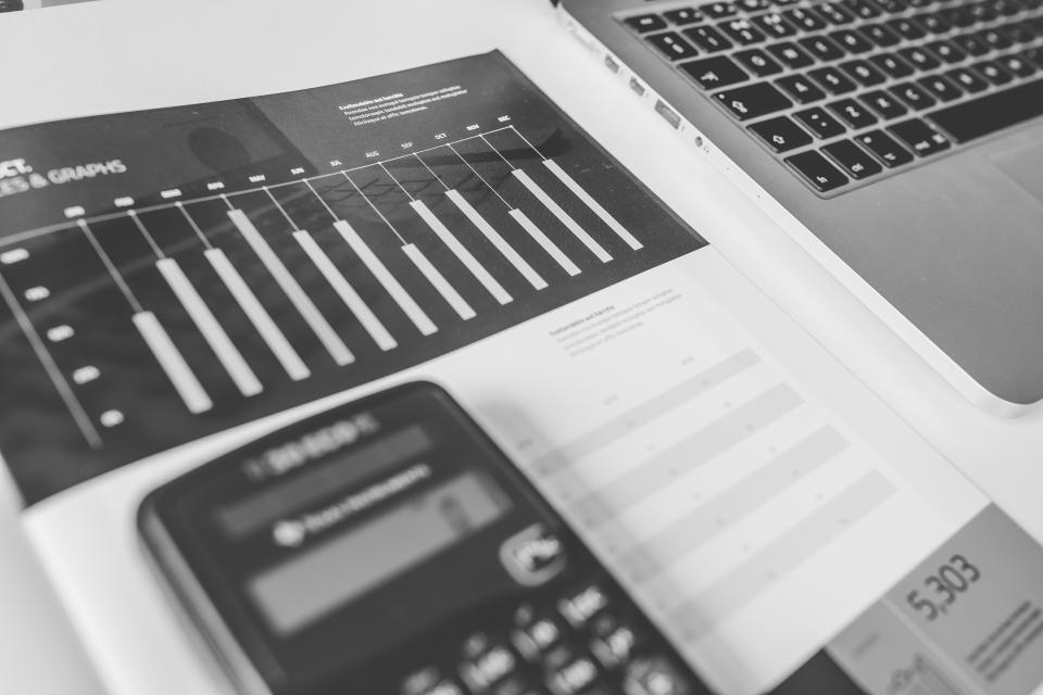 Black and white printout of bar charts next to a calculator and a laptop